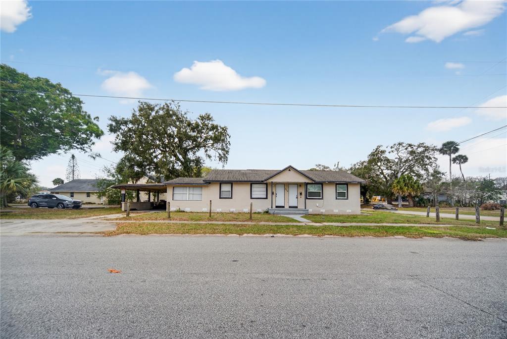 A single-story duplex with a carport sits behind a grassy yard under a blue sky — 514 S GRANNIS AVENUE, TITUSVILLE, FL