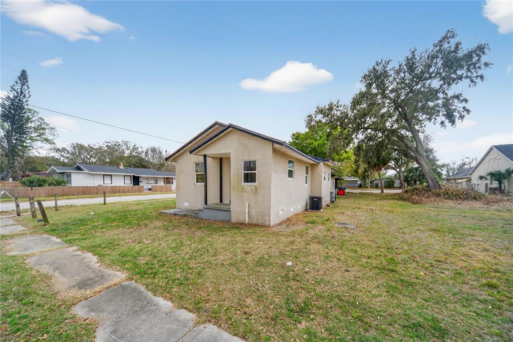 A small, single-story stucco house sits on a grassy lot under a blue sky — 514 S GRANNIS AVENUE, TITUSVILLE, FL