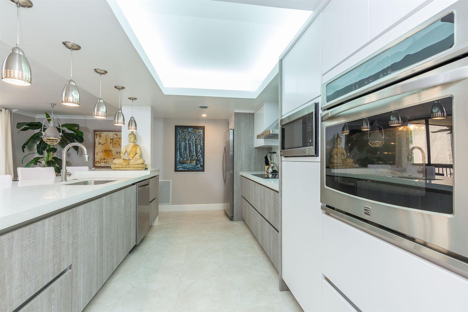 A modern kitchen features light wood cabinetry, white countertops, stainless steel appliances, and pendant lighting — 2455 Lindell Boulevard # 3304, Delray Beach FL 33444, DELRAY BEACH, FL