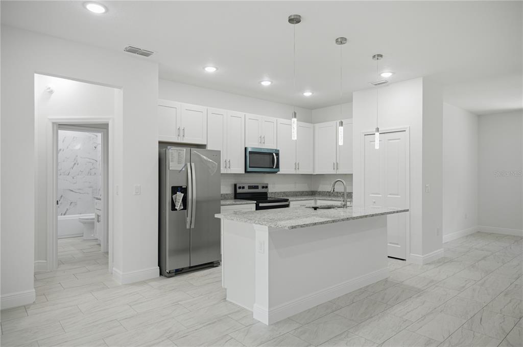 A modern kitchen features white cabinets, stainless steel appliances, a granite island, and tiled floors — 10735 N MALVA WAY DRIVE, CITRUS SPRINGS, FL