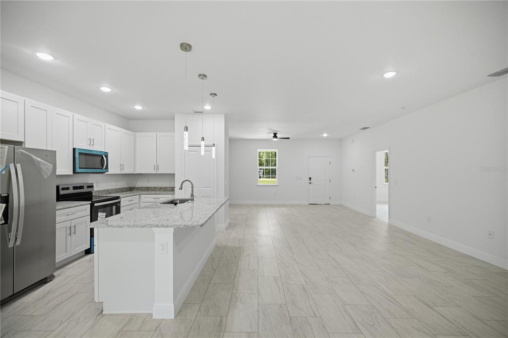 A modern kitchen with white cabinets and granite countertops opens into a spacious living area — 10735 N MALVA WAY DRIVE, CITRUS SPRINGS, FL