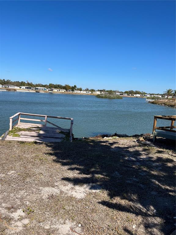 A wooden dock sits on the grassy bank overlooking a calm lake and distant homes — 2820 PENGUIN LANE, ENGLEWOOD, FL