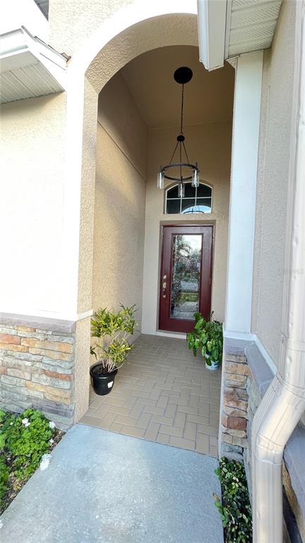 A covered entryway features a brick-paved floor, a dark red front door, and a hanging chandelier — 14112 QUEENSIDE ST, ORLANDO, FL