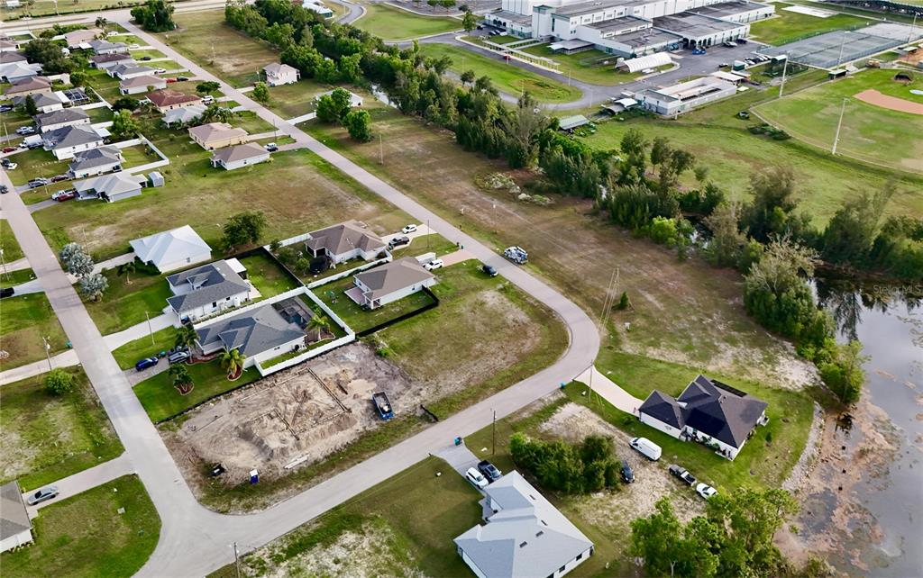 An aerial view shows several suburban houses, a construction site, and a pond — 3829 NE 23RD AVENUE, CAPE CORAL, FL