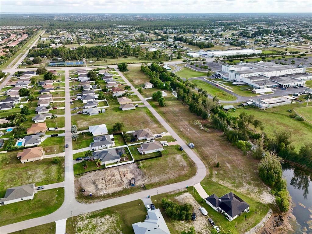 An aerial view shows a suburban neighborhood with houses, vacant lots, and a large commercial building — 3829 NE 23RD AVENUE, CAPE CORAL, FL