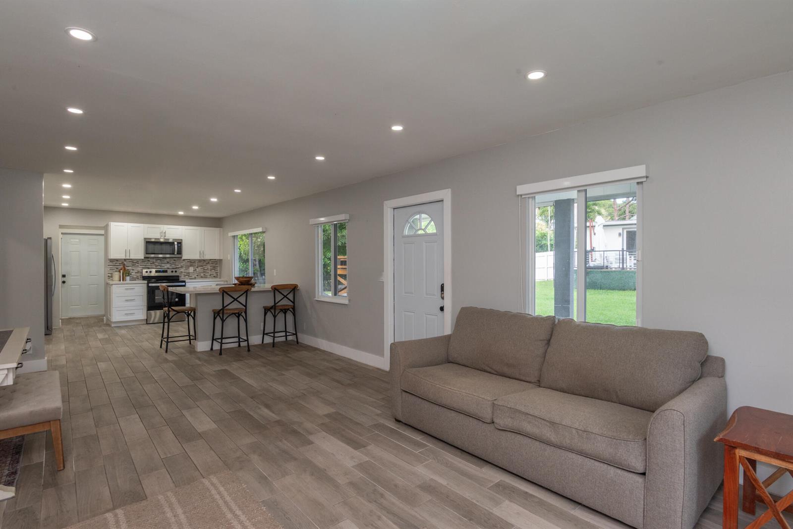 An open-concept living room and kitchen featuring gray tile floors, white cabinets, and a sofa — 13487 Barwick Road # B, Delray Beach FL 33445, DELRAY BEACH, FL