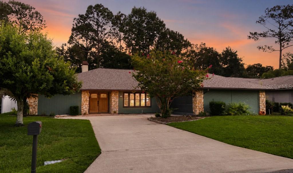 A single-story house with a green exterior, stone accents, and a concrete driveway at sunset — 31 PENNSYLVANIA LANE, PALM COAST, FL