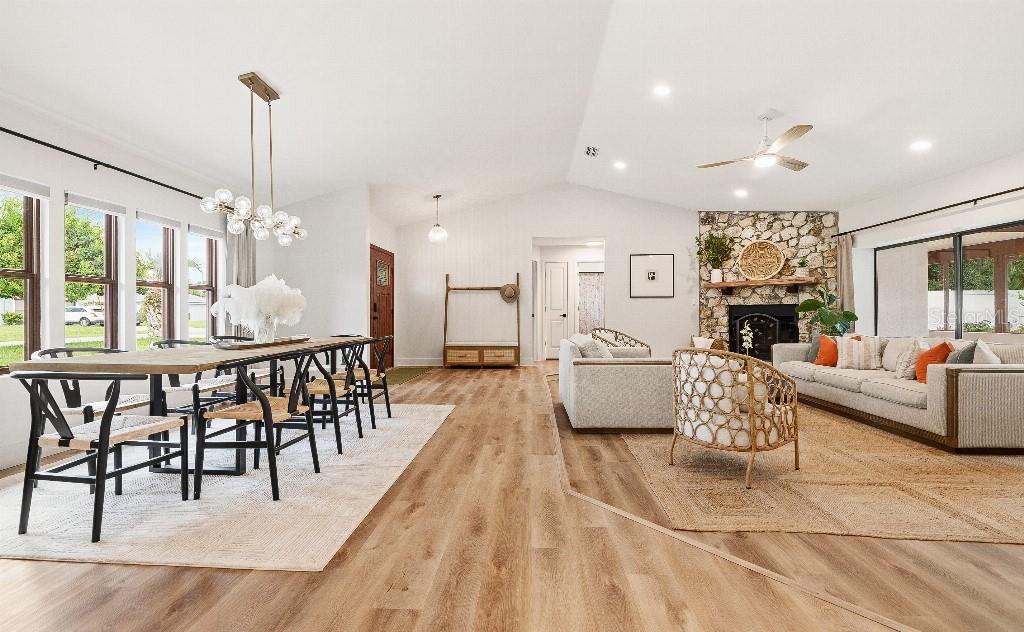 An open-concept living and dining area with wood-look flooring, a stone fireplace, and vaulted ceilings — 31 PENNSYLVANIA LANE, PALM COAST, FL