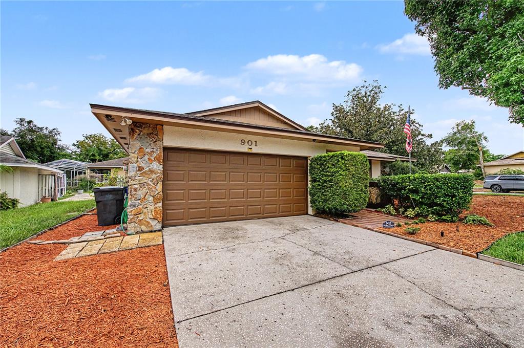A single-story house exterior features a brown garage door, stone siding, and a concrete driveway — 901 TARAWOOD LANE, VALRICO, FL