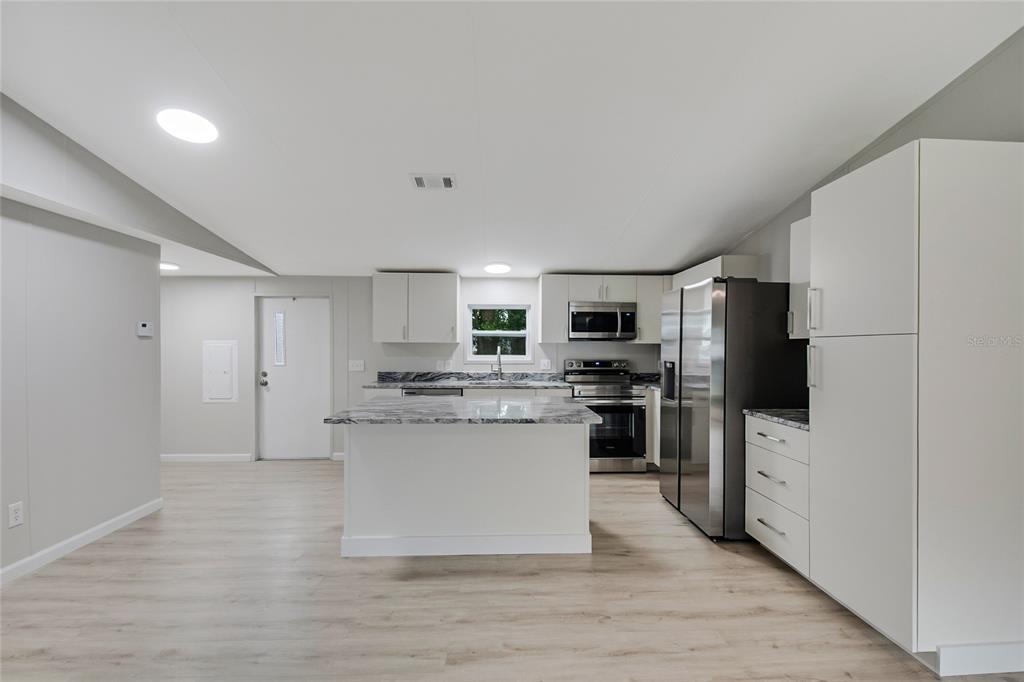 A modern kitchen features white cabinetry, a marble-topped island, and stainless steel appliances — 4321 SPARTAN DRIVE, ORLANDO, FL