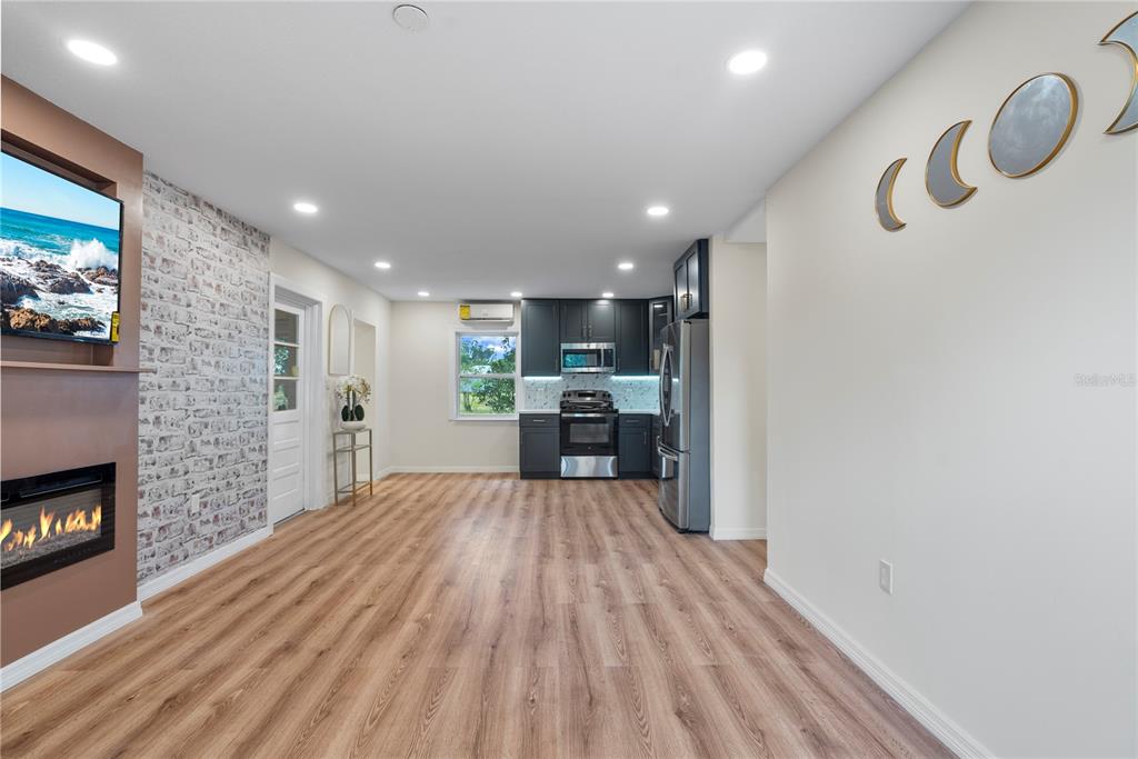 A kitchen and living area featuring dark cabinets, wood-look flooring, and a brick-patterned accent wall — 607 WALNUT DRIVE, FORT MEADE, FL