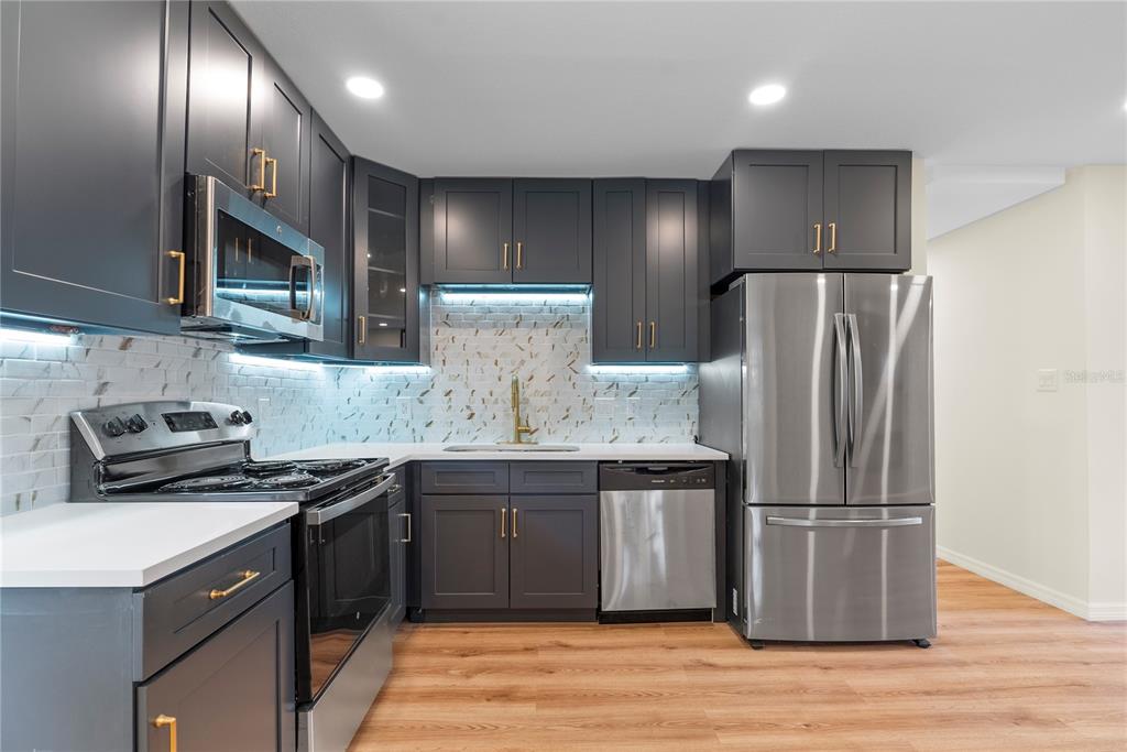 A modern kitchen features dark gray cabinets, stainless steel appliances, and a white tiled backsplash — 607 WALNUT DRIVE, FORT MEADE, FL