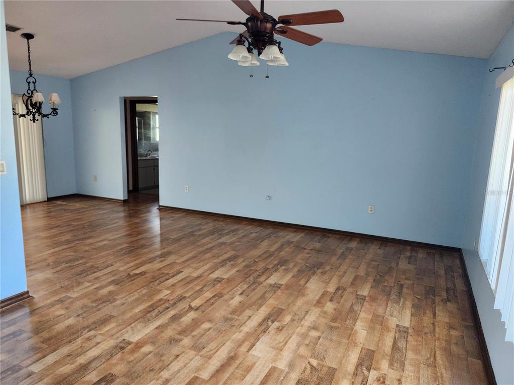 A living room with light blue walls, wood-look flooring, a ceiling fan, and a chandelier — 10115 HAYWARD ROAD, SPRING HILL, FL