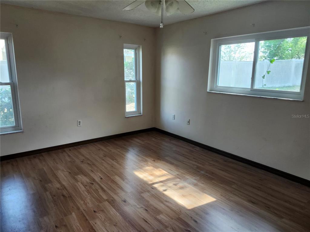 An empty bedroom features light-colored walls, wood-look flooring, and three windows — 10115 HAYWARD ROAD, SPRING HILL, FL