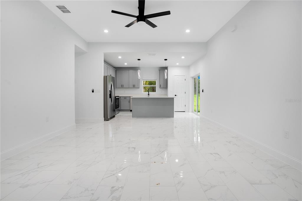 An open-concept kitchen and living area features white marble-look tile flooring and gray cabinetry — 1903 VAN ALLEN CIRCLE, DELTONA, FL