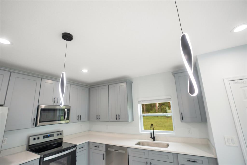 A kitchen features light gray cabinets, stainless steel appliances, white countertops, and two modern pendant lights — 1903 VAN ALLEN CIRCLE, DELTONA, FL