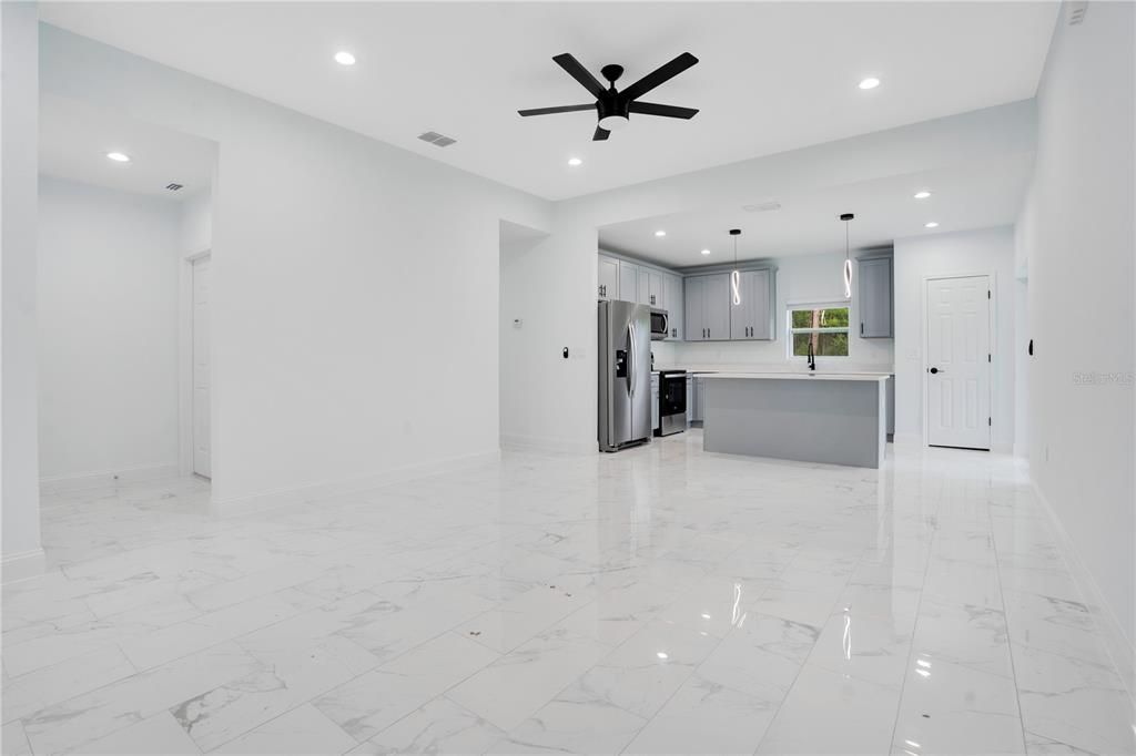 An open-concept kitchen and living area features white walls, marble-look tile flooring, and gray cabinetry — 1903 VAN ALLEN CIRCLE, DELTONA, FL