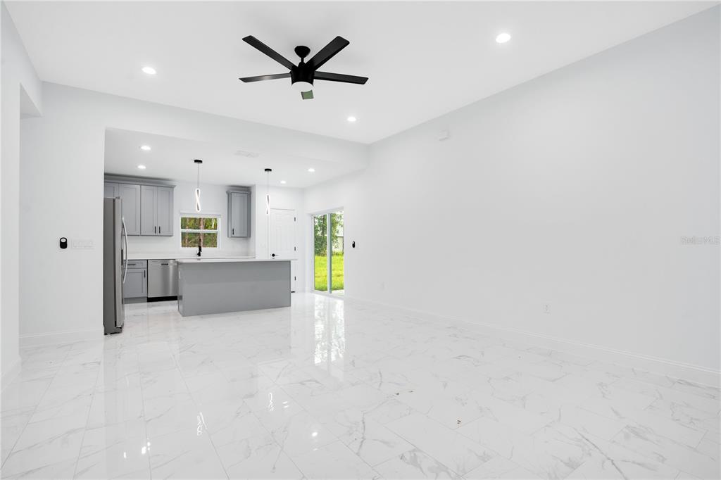 A bright, open-concept kitchen and living area features white marble-look tile floors and gray cabinetry — 1903 VAN ALLEN CIRCLE, DELTONA, FL
