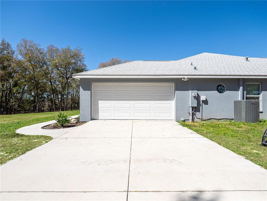 A gray house exterior features a white two-car garage door and a concrete driveway — 10688 SW 129TH TERRACE ROAD, DUNNELLON, FL