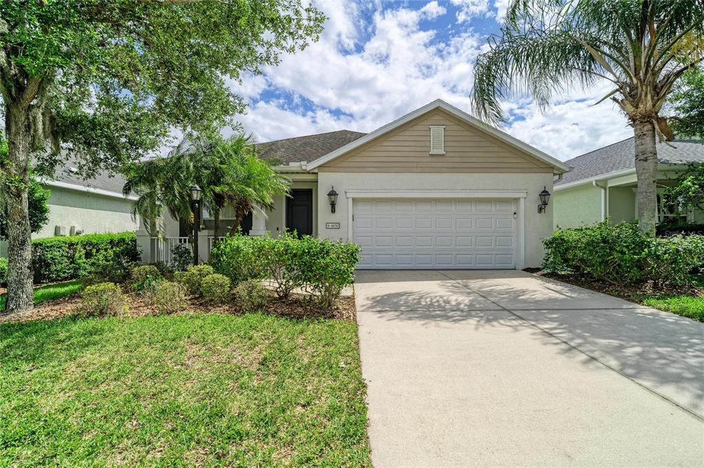 A single-story house with a white garage, beige siding, and a landscaped front yard — 4650 WOODBROOK DRIVE, SARASOTA, FL
