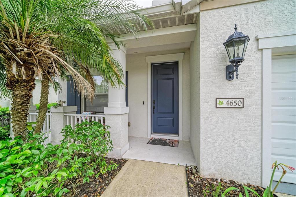 A blue front door sits under a covered entryway next to a palm tree — 4650 WOODBROOK DRIVE, SARASOTA, FL