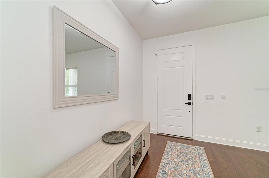 An entryway features a light wood console table, a wall mirror, and a patterned rug — 4650 WOODBROOK DRIVE, SARASOTA, FL
