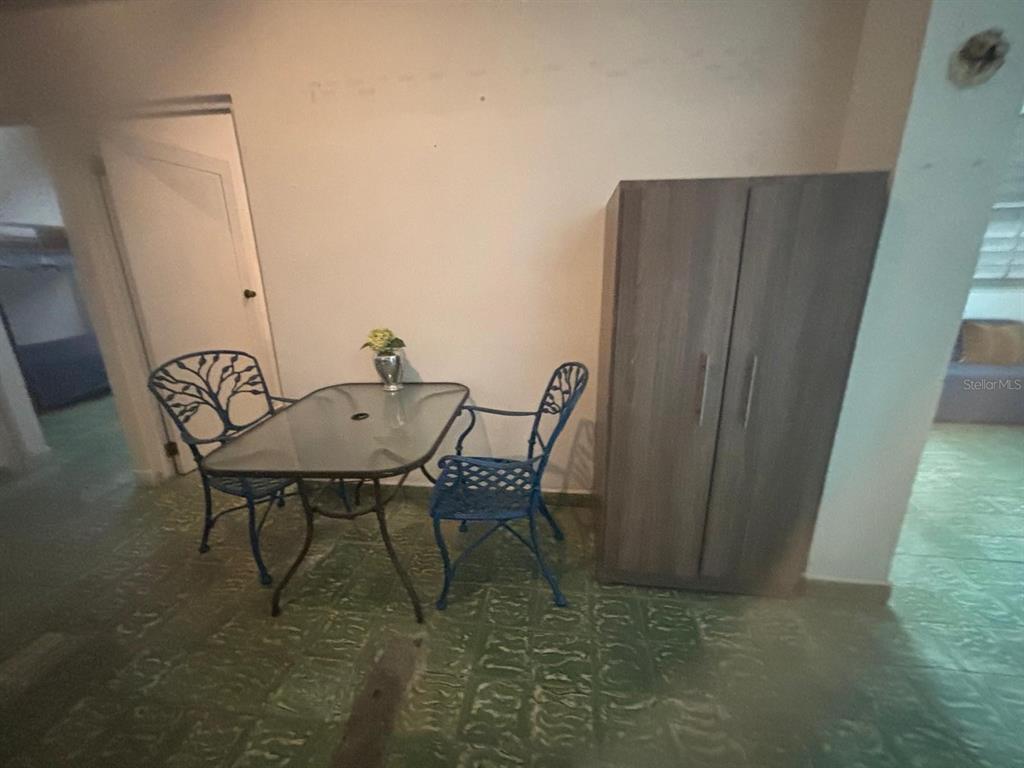 A dining area features a glass-topped table, two blue metal chairs, and a wooden wardrobe — 26 MANUEL CORCHADO, AGUADILLA, PR