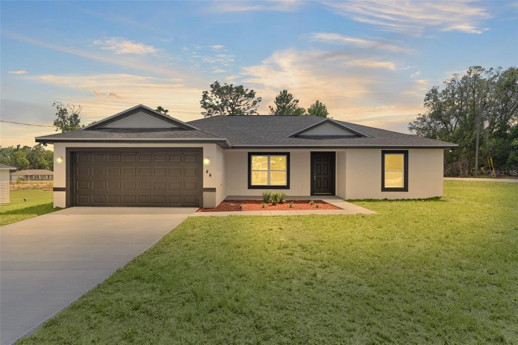 A single-story house with a dark garage door, white exterior, and a front lawn — 44 MALAUKA DRIVE, OCKLAWAHA, FL