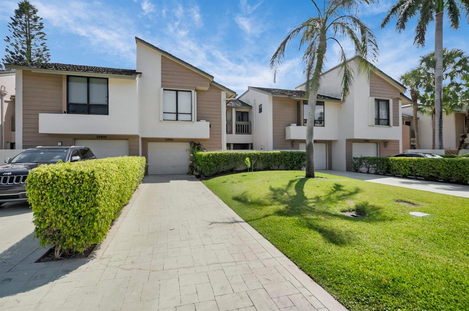 A two-story townhouse exterior with a paved driveway, green hedges, and a palm tree — 22922 Ironwedge Drive, Boca Raton FL 33433, BOCA RATON, FL