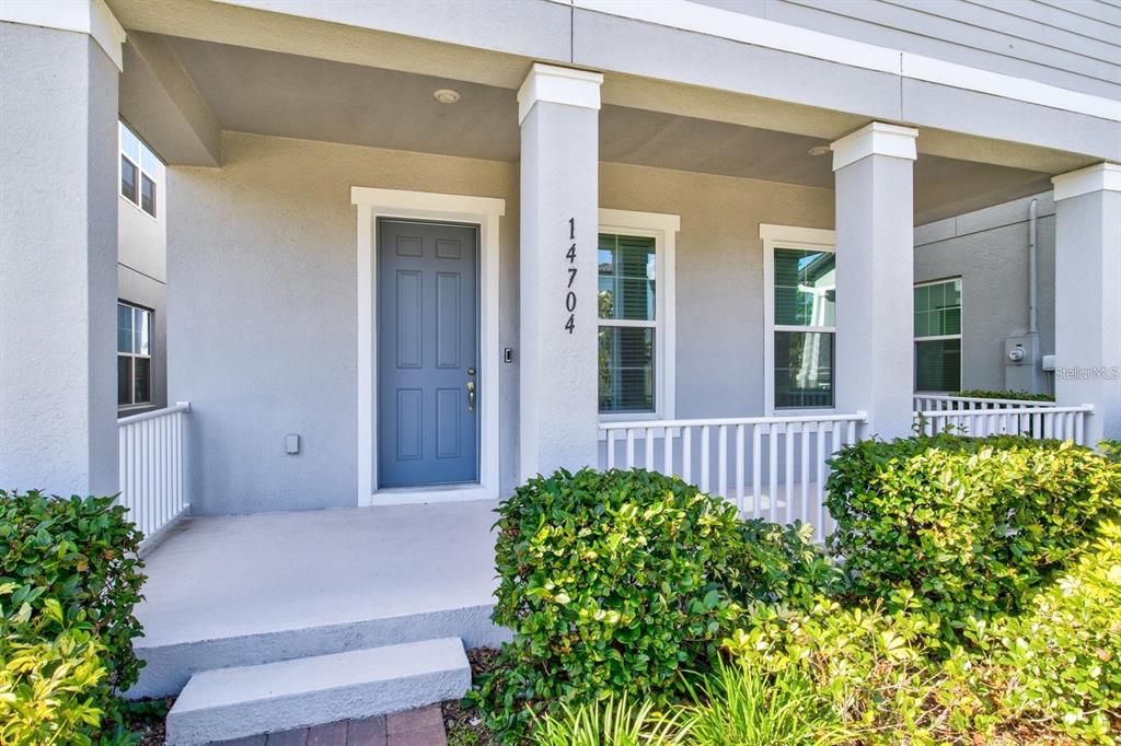 The exterior of a house features a blue front door, white railings, and green bushes — 14704 SETON CREEK BOULEVARD, WINTER GARDEN, FL
