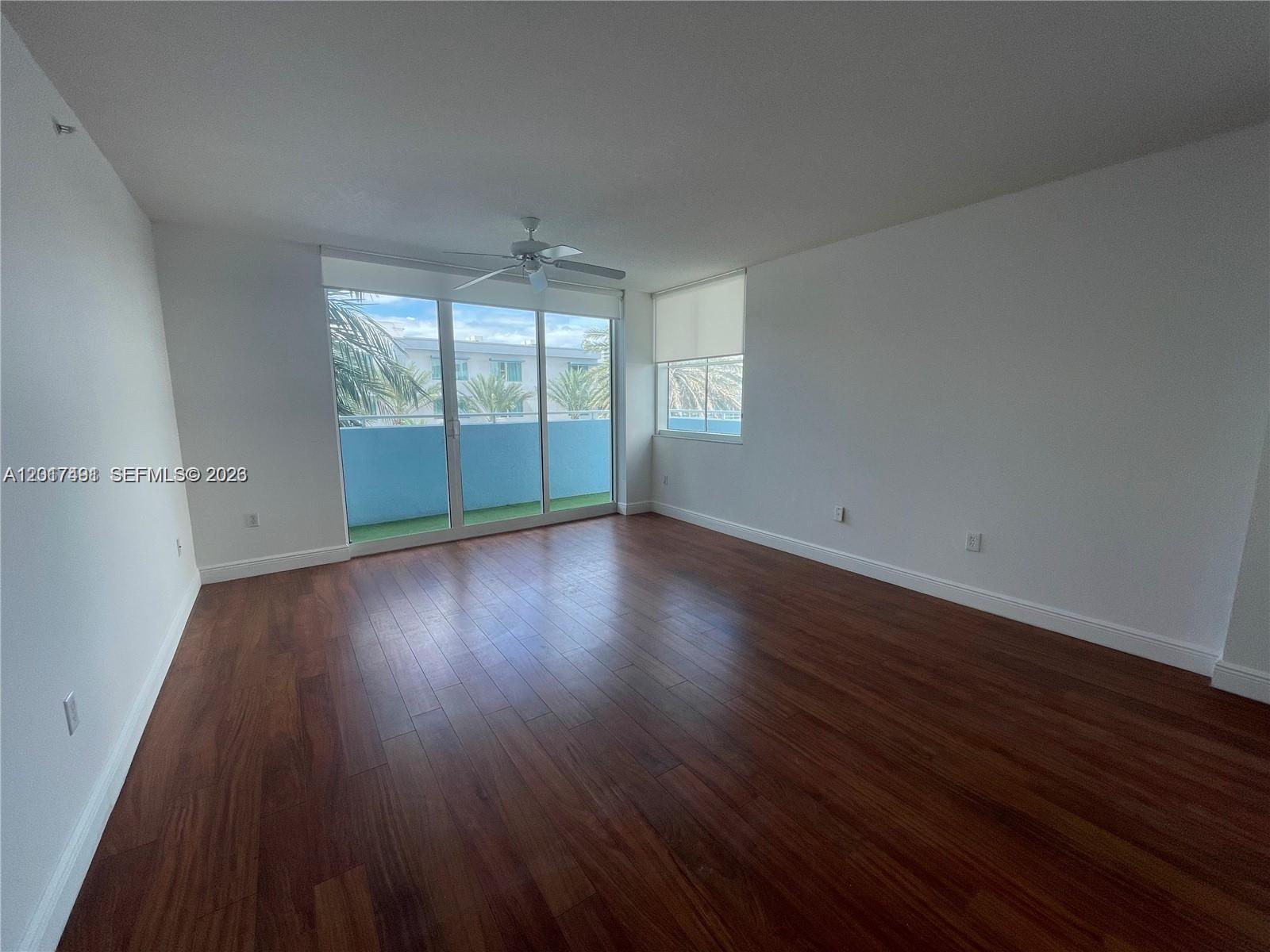 An empty room features dark wood flooring, white walls, a ceiling fan, and sliding glass doors — 9201 Collins Ave # 321, Surfside FL 33154, SURFSIDE, FL