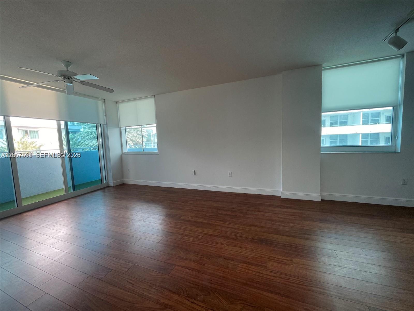 An empty room features dark wood flooring, white walls, a ceiling fan, and large windows — 9201 Collins Ave # 321, Surfside FL 33154, SURFSIDE, FL
