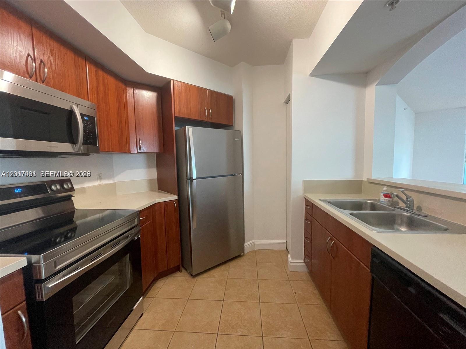 A kitchen features wood cabinets, stainless steel appliances, and beige tile flooring — 9201 Collins Ave # 321, Surfside FL 33154, SURFSIDE, FL