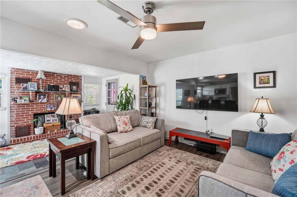 A living room features a brick fireplace, two sofas, a ceiling fan, and a wall-mounted television — 2680 ROBIN AVENUE, KISSIMMEE, FL