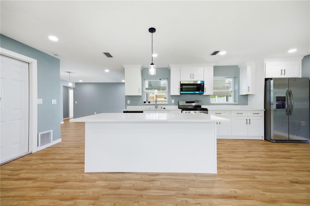 A modern kitchen features white cabinets, a central island, stainless steel appliances, and wood flooring — 5920 DENVER STREET NE, ST PETERSBURG, FL