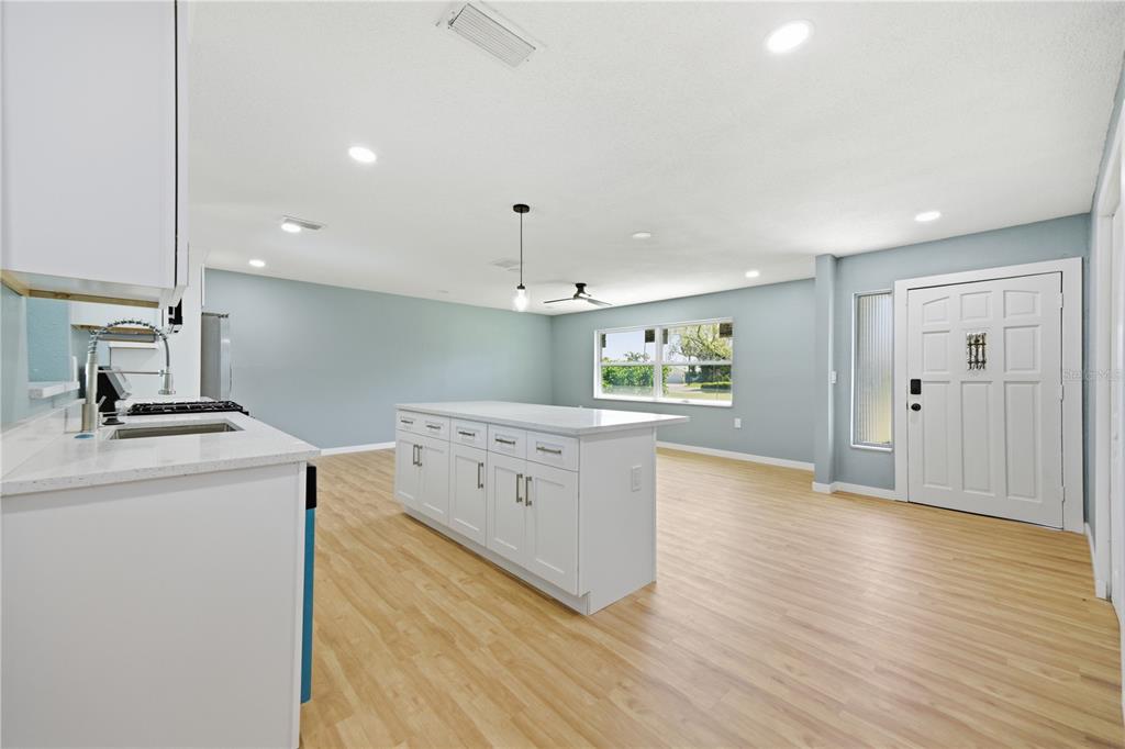 A kitchen with a white island and light wood flooring opens into a living area — 5920 DENVER STREET NE, ST PETERSBURG, FL
