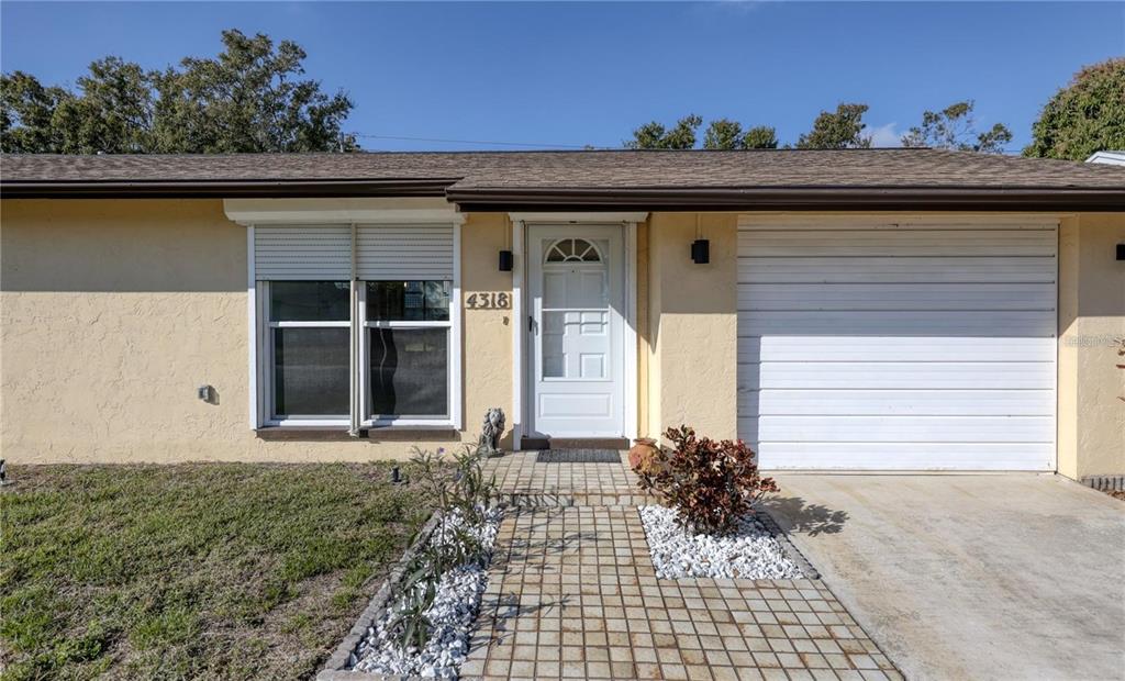 The exterior of a single-story house features a white front door, garage, and paved walkway — 4318 GREAT LAKES DRIVE N, CLEARWATER, FL