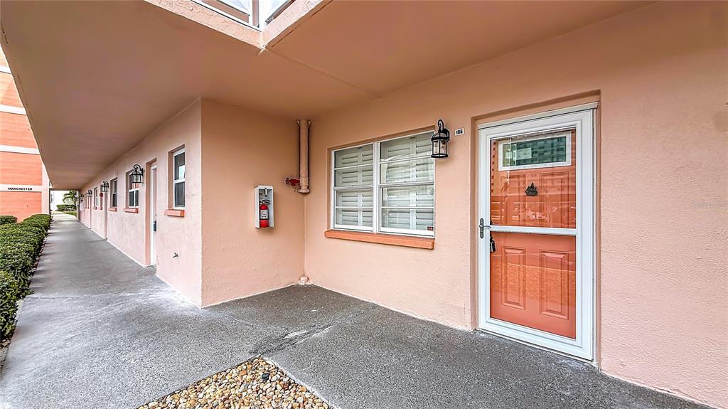 An exterior view of a peach-colored building with a walkway, a door, and windows — 6025 SHORE BOULEVARD S UNIT 106, GULFPORT, FL