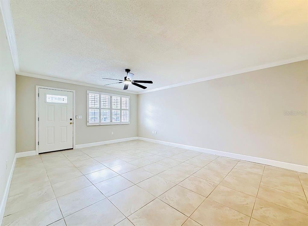 A bright, empty room features light-colored tile flooring, white walls, a ceiling fan, and shutters — 6025 SHORE BOULEVARD S UNIT 106, GULFPORT, FL