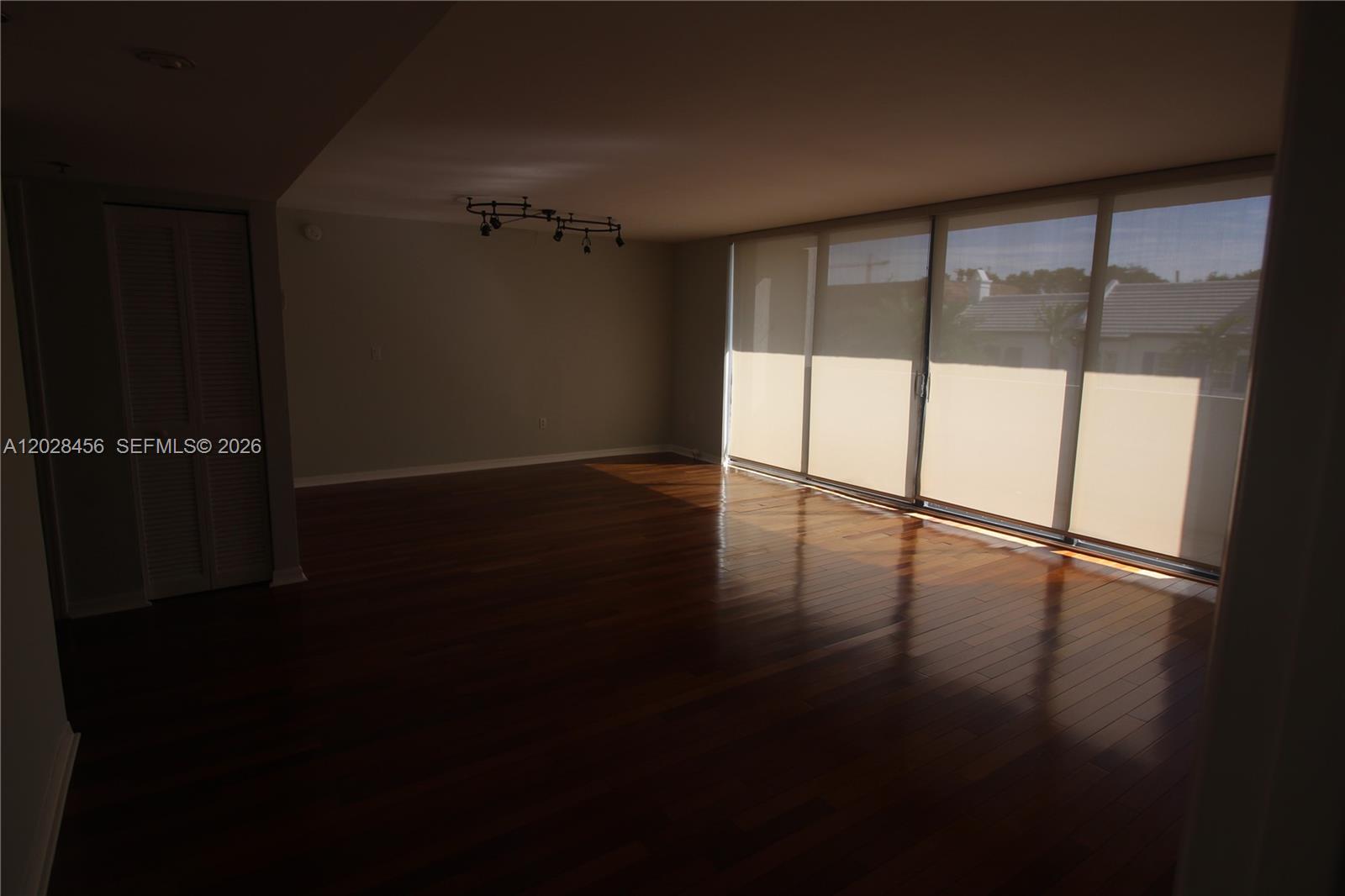 An empty room features dark hardwood floors, a track lighting fixture, and large sliding glass doors — 441 Valencia Ave # 202, Coral Gables FL 33134, CORAL GABLES, FL