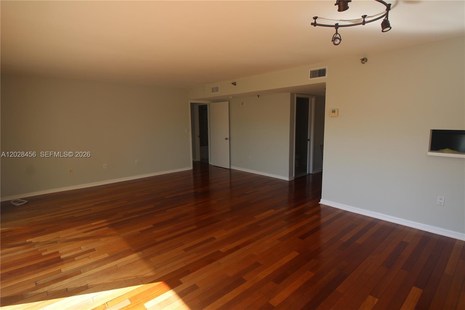 An empty room features dark hardwood flooring, light-colored walls, and a modern track lighting fixture — 441 Valencia Ave # 202, Coral Gables FL 33134, CORAL GABLES, FL