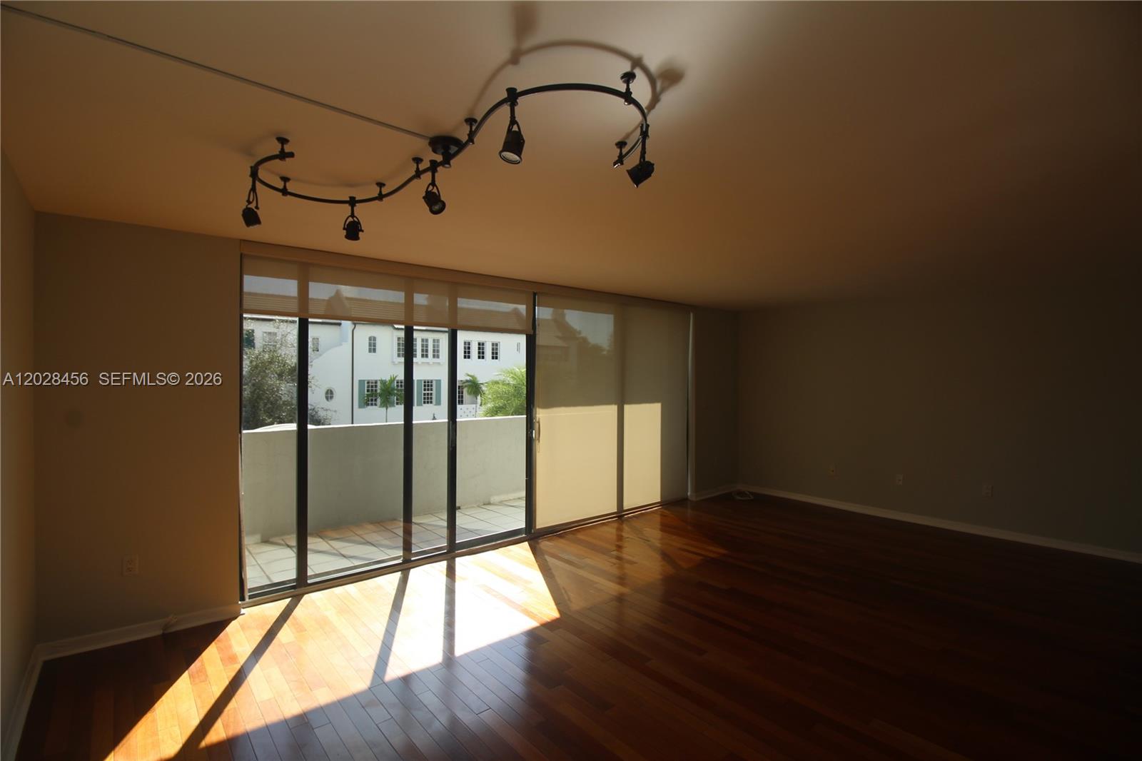 An empty room features hardwood floors, a curved track lighting fixture, and sliding glass doors — 441 Valencia Ave # 202, Coral Gables FL 33134, CORAL GABLES, FL