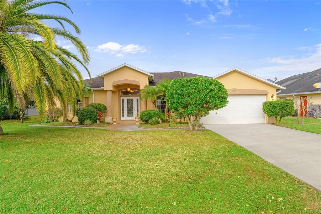 A single-story tan house with a white garage door, front entryway, and a large palm tree — 16 LONDON DRIVE, PALM COAST, FL