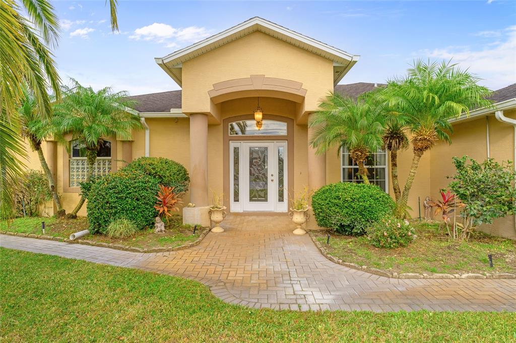 A tan house exterior features a paved walkway leading to a white front door — 16 LONDON DRIVE, PALM COAST, FL