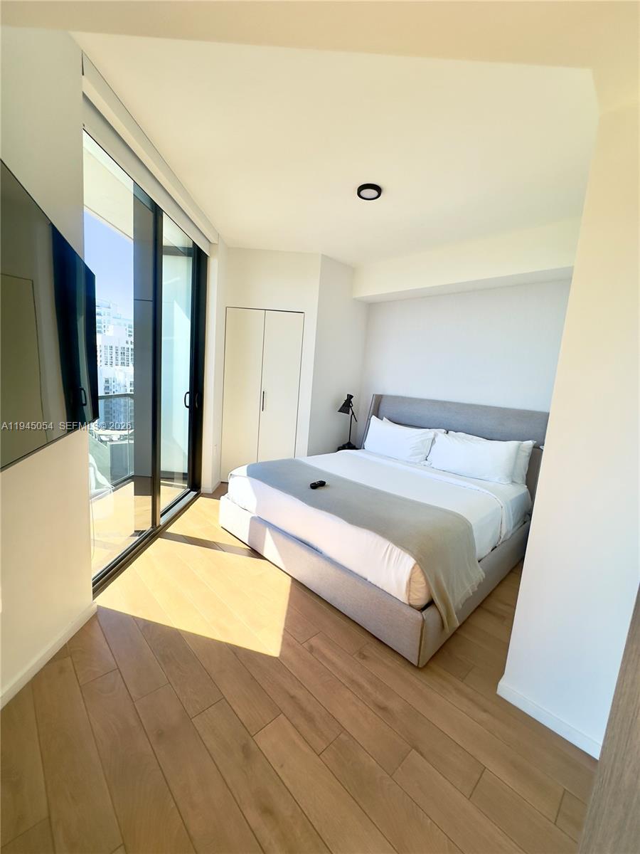 A modern bedroom features a gray upholstered bed, light wood flooring, and floor-to-ceiling windows — 398 NE 5th St # 2114, Miami FL 33132, MIAMI, FL