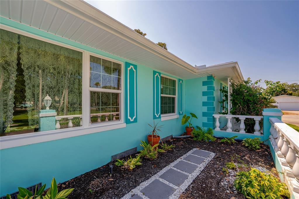 A bright turquoise house exterior features white window shutters, a stone walkway, and a balustrade — 697 JOHN ANDERSON DRIVE, ORMOND BEACH, FL