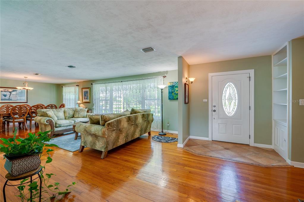 A living room with hardwood floors, a patterned sofa, and an entryway with a white door — 697 JOHN ANDERSON DRIVE, ORMOND BEACH, FL