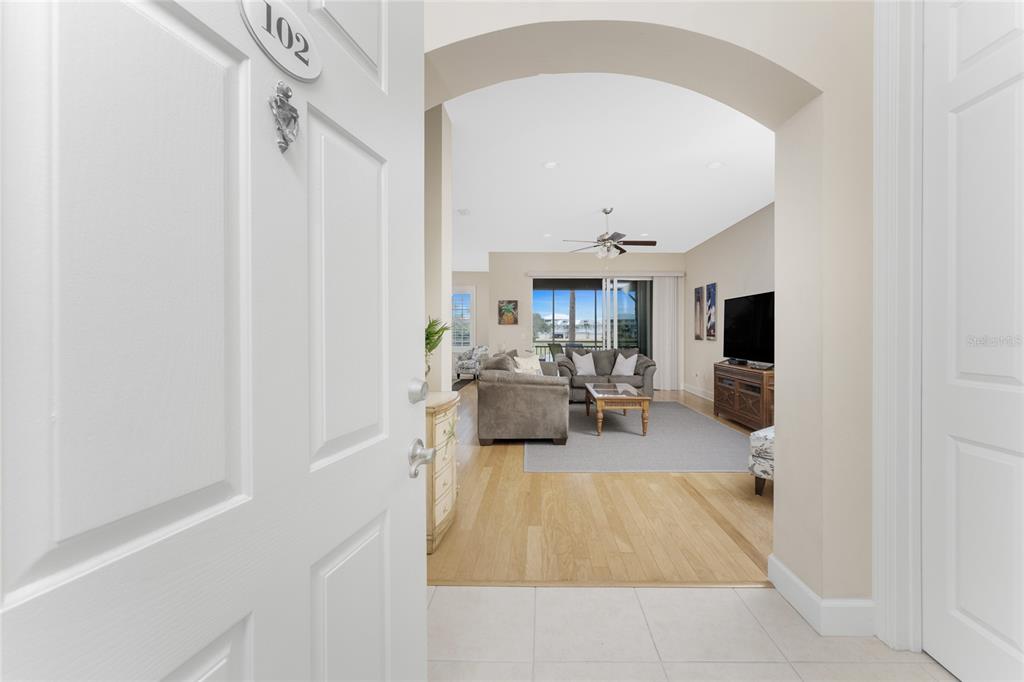 A view from an entryway into a living room with hardwood floors and a balcony — 10641 LEMON CREEK LOOP UNIT 102, ENGLEWOOD, FL