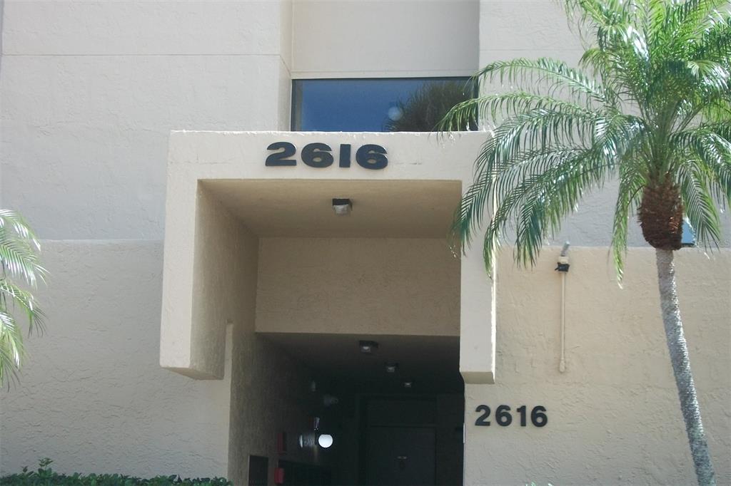 The exterior entrance of a beige building features the number 2616 and a palm tree — 2616 COVE CAY DRIVE UNIT 207, CLEARWATER, FL