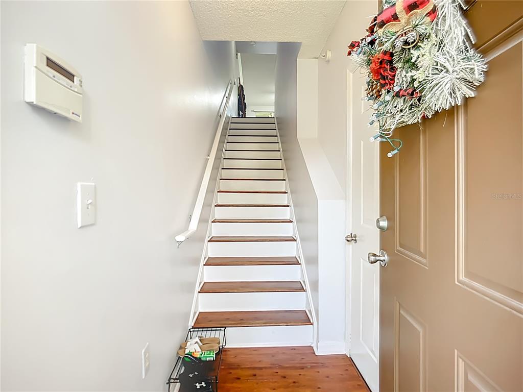 An entryway features a wooden front door, a staircase with white risers, and hardwood flooring — 4990 BARALDI CIRCLE UNIT 209, SARASOTA, FL